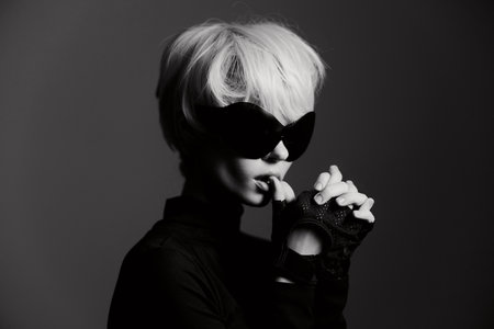 Stylish woman in black outfit with sunglasses and fingerless gloves, posing dramatically with a...