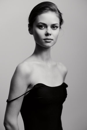 Elegant young woman with a natural look, wearing a strapless black dress, posing with confidence....