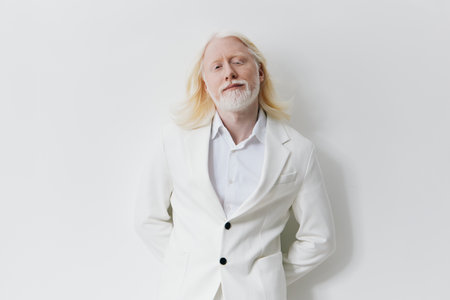 Stylish man in a white suit with long hair posing against a neutral background, exuding confidence...