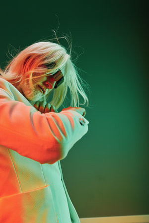 Creative portrait of a person with long hair in a stylish suit, captured against a vibrant green and orange background, highlighting modern fashion and artistic expressionの写真素材