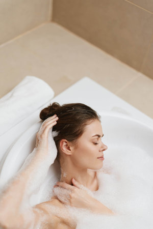 Relaxed woman enjoying a bubble bath, gently touching her hair with a serene expression on her face. Spa and self-care concept with a calming atmosphere.の写真素材