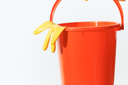 Orange bucket, yellow gloves and a rubber glove on a white backgroundの写真素材