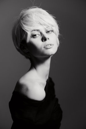 Elegant young woman with short white hair posing gracefully in a minimalist black and white setting....