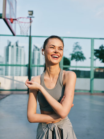 Young woman enjoying a sunny day at the basketball court, smiling radiantly in athletic wearの写真素材