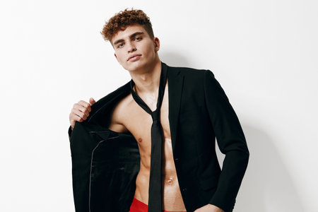Confident young man in a black suit jacket, holding it open, showcasing his toned physique. Elegant...