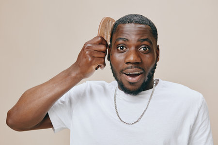 Happy man using a comb in a light colored background, displaying surprise and joy in his expression, showcasing a stylish hairstyle with a casual white t shirtの写真素材