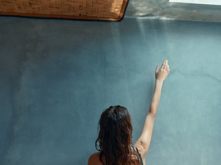 Woman reaching out to touch the sunlit wall of a room with a window in itの写真素材