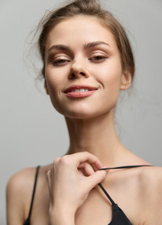Confident young woman posing with a subtle smile, wearing a black top, against a neutral gray background. Embracing natural beauty and self-assurance.の写真素材