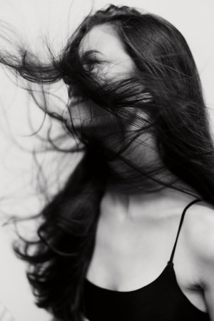 Black and white portrait of a woman with long hair flowing in motion, expressing freedom and confidence against a neutral background. Emotional and artistic concept.の写真素材