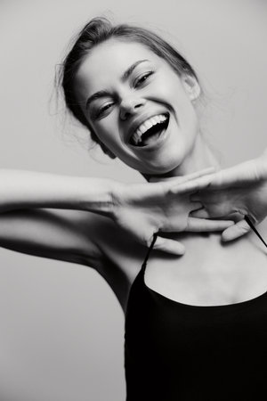 Joyful young woman laughing joyfully, hands raised playfully around her face. Black and white portrait highlighting happiness and carefree emotions.の写真素材