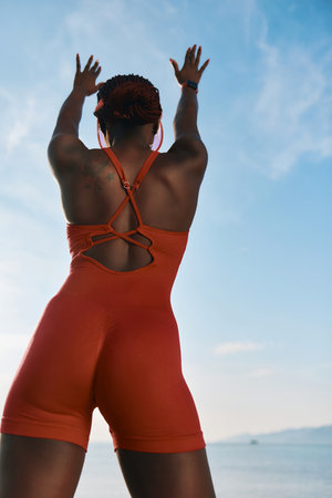 Silhouette of a woman in an orange bodysuit stretching against a bright blue skyの写真素材