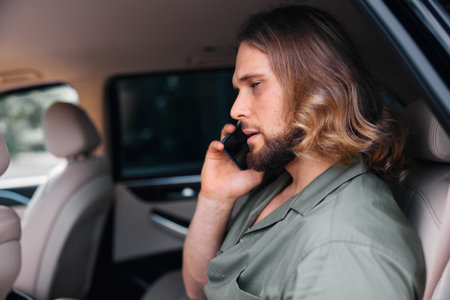 Young man talking on phone in car interior with relaxed expression