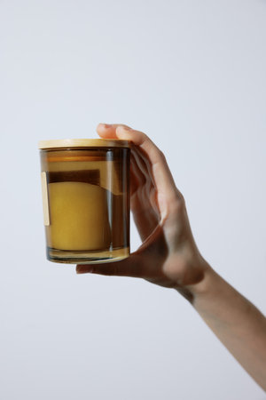 Hand holding glass jar with candle inside on white background, with candle and candle holder written on itの写真素材