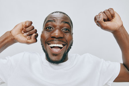 Excited man showing joy and enthusiasm with raised hands, smiling widely on a light background,...