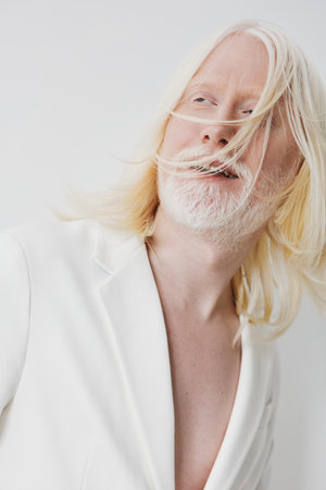 portrait of a stylish man with long blonde hair and a beard, dressed in a white suit, against a minimalist white background, exuding confidence and elegance in a contemporary fashion styleの写真素材