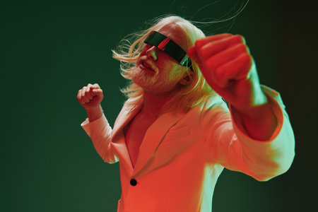 Stylish man dancing with futuristic glasses in a vibrant setting, showcasing a blend of retro and modern fashion with dramatic lighting The background features green and red tonesの写真素材