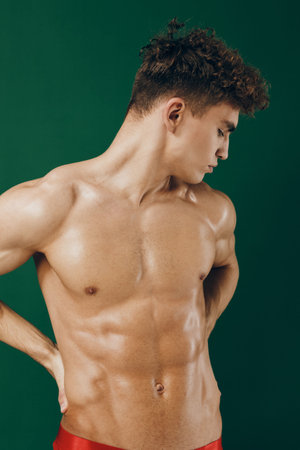 Muscular young man posing with confidence against a green background, showcasing strong physique and...