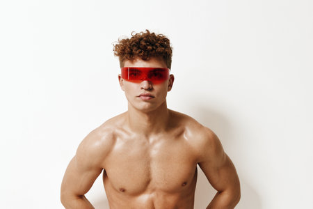 Stylish young man with curly hair wearing red sunglasses, posing confidently against a plain white background. Fashion and modern lifestyle concept.の写真素材