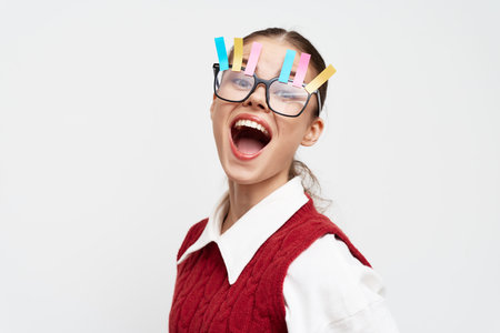 cheerful girl with oversized glasses, colorful clips, and a joyful expression wearing a red vest against a white background, portraying creativity and fun in a playful conceptの写真素材