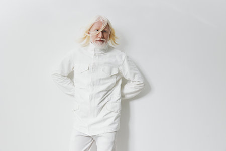 Fashionable elderly man in a stylish white outfit against a minimalist white background, embodying...