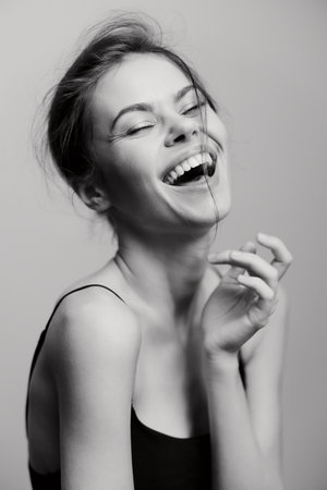 Joyful young woman laughing heartily, showcasing genuine happiness against a soft grey background. Emotion and positivity concept radiating through a monochrome palette.の写真素材