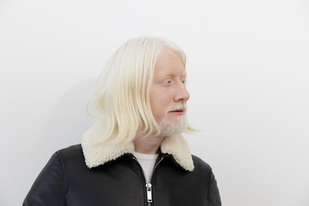 Portrait of a man with long white hair and beard, wearing a black leather jacket against a simple white background, showcasing confidence and modern style in a minimalist settingの写真素材