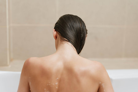Relaxed woman bathing in a modern bathroom, her back turned while enjoying a moment of tranquility. Wellness and self-care concept highlighted.の写真素材