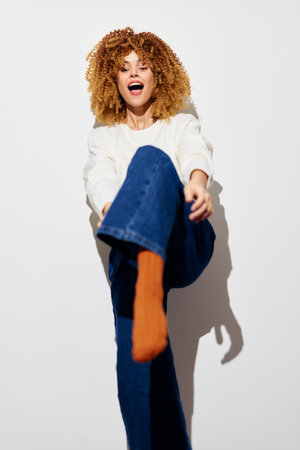 Cheerful young woman posing playfully against a clean white background, showcasing her outfit and vibrant personality with joy and energy Her curly hair and colorful socks add flairの写真素材