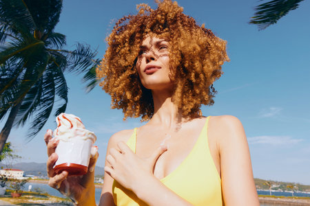 Young woman with curly hair enjoying ice cream under a clear blue sky surrounded by palm trees A bright summer day conveys a carefree vibeの写真素材