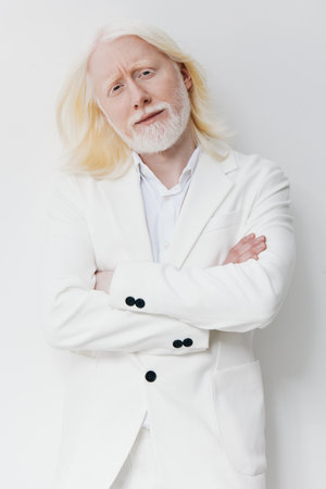 Stylish man in a white suit with a thoughtful expression, standing against a clean white background His long white hair and beard add a unique charm to the sophisticated lookの写真素材
