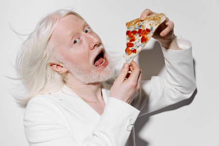 Excited man with white hair and beard eating pizza slice against a plain white background, conveying...
