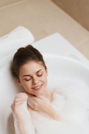 Relaxed woman enjoying a bubble bath in a modern bathroom, smiling with closed eyes, conveying calmness and self-care. Home relaxation and wellness concept.の写真素材
