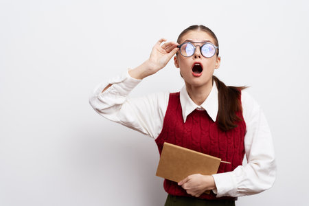 surprised woman with glasses holding a book on a plain white background, looking astonished and curious, wearing a red sweater, conveying shock or realizationの写真素材