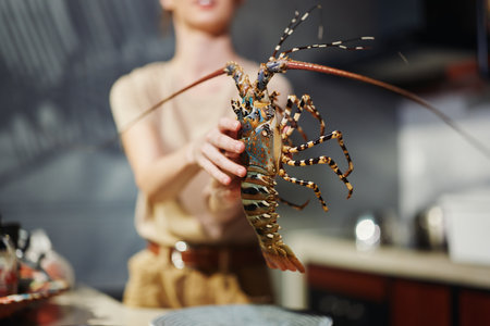 Woman holding lobster in kitchen, preparing seafood dish with fresh ingredientsの写真素材