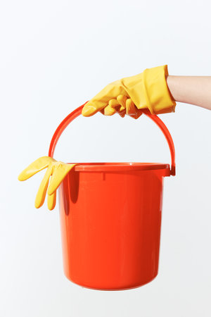 Womans hand holding orange bucket with yellow rubber glove on white background