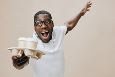 Happy young man holding coffee cups with excitement, wearing casual white shirt and glasses, joyful expression on a neutral beige background, capturing the essence of celebration and positivityの写真素材