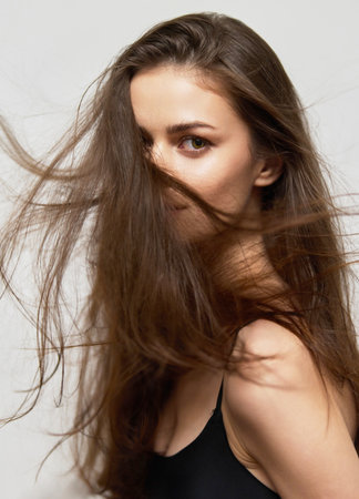 Young woman with long flowing hair looking at the camera, capturing a sense of movement and elegance. Beauty and self-expression in a minimalist setting.の写真素材