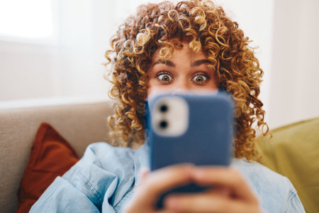 Happy woman on sofa, holding mobile phone, enjoying online relaxation gameの写真素材