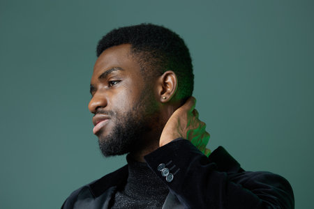 Stylish bearded man in black jacket and turtleneck sweater posing confidently against urban backdropの写真素材