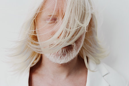 Portrait of a serene middle aged man with long, flowing hair partially obscuring his face against a soft, light background The image captures a calm and introspective moodの写真素材