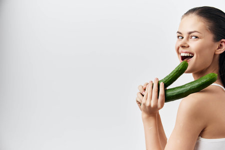 Smiling woman holding cucumbers in front of a white background, showcasing playful emotions and healthy lifestyle Fresh vegetables and vibrant expressions highlight joy and healthの写真素材