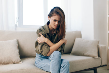 Stressed Woman on Couch, Feeling Sad and Worried, Experiencing Mental Health Anxiety at Home: Depressed Mood in Despair.の写真素材