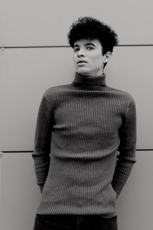 Fashionable young man in a black and white turtleneck sweater posing against a wall with hands on hipsの写真素材