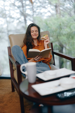 Young woman reading a book in a cozy armchair, enjoying a moment of relaxation in a serene natural...