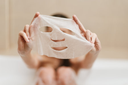 Relaxed woman holding a facial mask while enjoying a bath, creating a spa-like atmosphere for self-care and beauty routines. Pampering and wellness concept.の写真素材