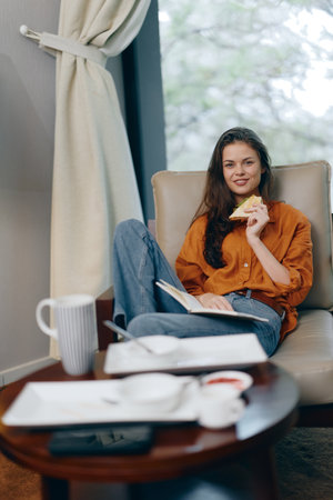 Young woman enjoying a healthy snack while relaxing indoors, wearing an orange shirt and jeans, surrounded by a calm atmosphere and natural lightの写真素材