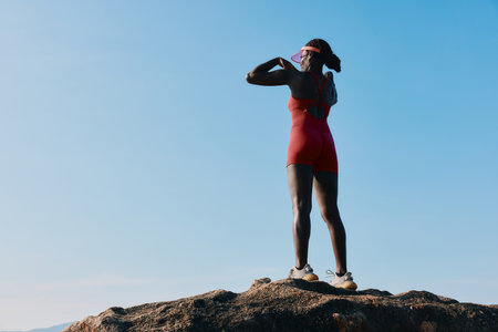 Woman stretching on a rock against a clear blue sky in athletic wearの写真素材