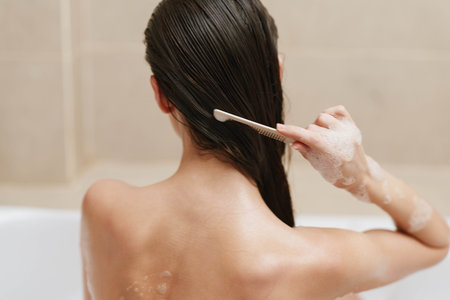 Relaxed woman combing her long, wet hair in the bathroom, surrounded by a serene atmosphere, focusing on personal care and self-pampering.の写真素材