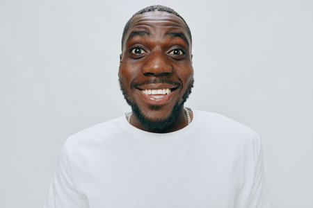 Smiling young man with joyful expression in casual white t shirt against light gray background, highlighting positivity and happiness Engaging portrait suitable for diverse themesの写真素材