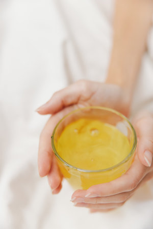 Woman holding bowl of yellow liquid on white bed sheet with white sheet on top